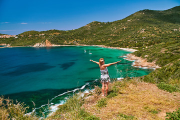 Happy smiling girl standing over the beautiful turquoise lagoon in Corsica - obrazy, fototapety, plakaty