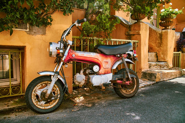 Fototapeta na wymiar Vintage rusty red small motorcycle next to orange facade
