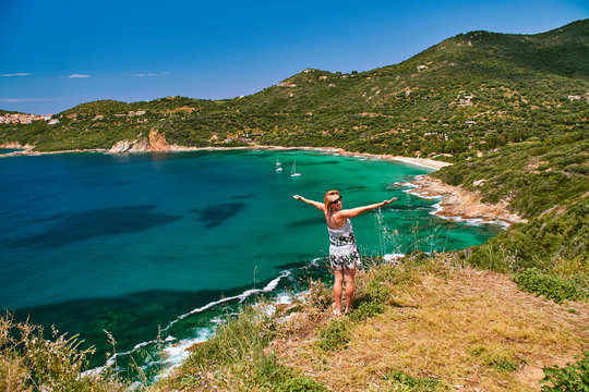 Happy smiling girl standing over the beautiful turquoise lagoon in Corsica