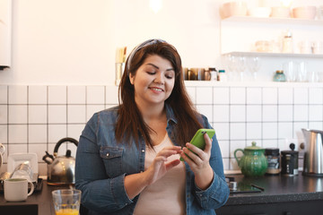 Cheerful beautiful young brunette overweight woman browsing social media on her mobile phone,...