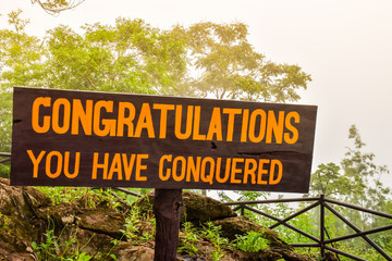 The sign that "congratulations you have conquered" on top of a hill.