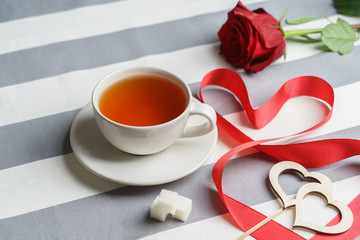 Romantic still life with a cup of tea and bright red holiday attributes.