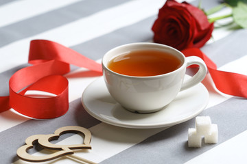 Romantic still life with a cup of tea and bright red holiday attributes.