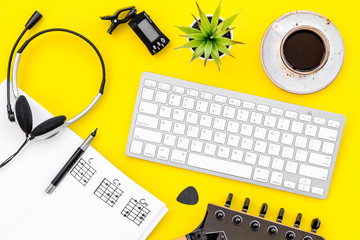Desk of musician for songwriter work with headphones, keyboard, guitar and notes yellow background top view