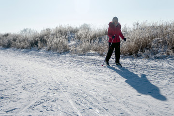 A girl in a red jacket and black pants on skis in the morning light. Snowy background with trails, shadow from woman and copyspace.