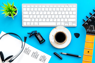 songwriter or dj work place with keyboard, coffee, guitar neck, notes and headphones on blue background top view