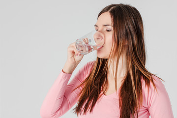 Young brunette woman drinking pure water isolated on grey backgr