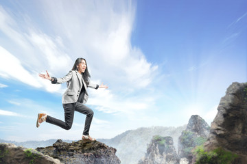 Young asian business woman in formal suit jumping on the top of mountain