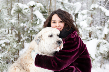 Portrait of beautiful young woman with her South Russian Shepherd Dog on a background of winter coniferous forest.