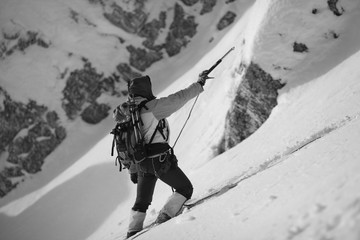 A climber on a snowy slope holds an ice ax in his hand, marking the path between the rocks. Black...