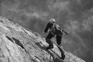 The climber climbs up the rock wall. Black and white.