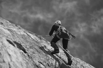 Foto op Aluminium The climber climbs up the rock wall. Black and white. © esalienko