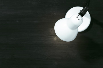 White office lamp on the black table background with copy space, top view.