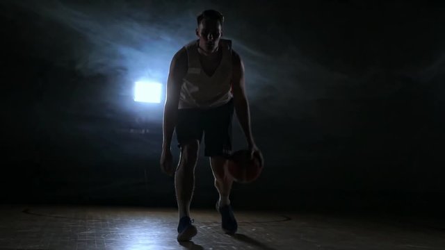 one young adult man, basketball player dribble ball, dark indoors basketball court. Slow motion