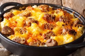 Hot Jolean's potato casserole, smoked sausages with cheese sauce close-up in a frying pan. horizontal