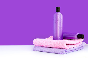 Obraz na płótnie Canvas two purple cosmetic bottles on two towels on a lilac background. Spa concept.