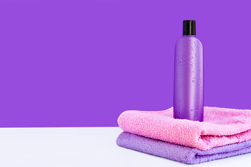 Obraz na płótnie Canvas one purple cosmetic bottle on two towels on a lilac background. Spa concept.
