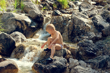 the child sits by the brook on the rocks in nature.