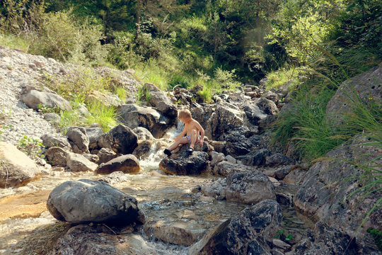 the child sits by the brook on the rocks in nature.