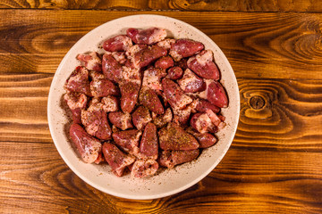 Ceramic plate with raw chicken hearts on wooden table. Top view
