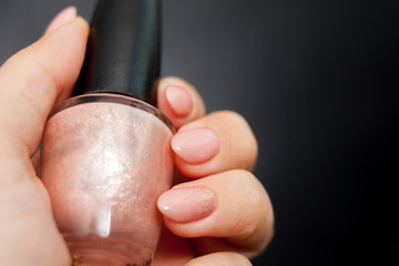 Nude manicure with gold decor. Womens hand holding a bottle of nail Polish