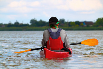 Rear view of teenager paddle red kayak on summer Danube river. Summer kayaking. Concept for adventure, travel, action, lifestyle