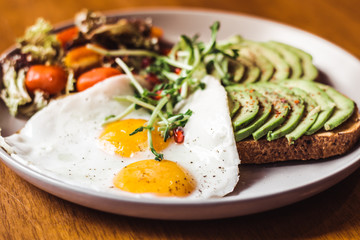 Toast with avocado on top, sunny side up egg and cherry tomato salad