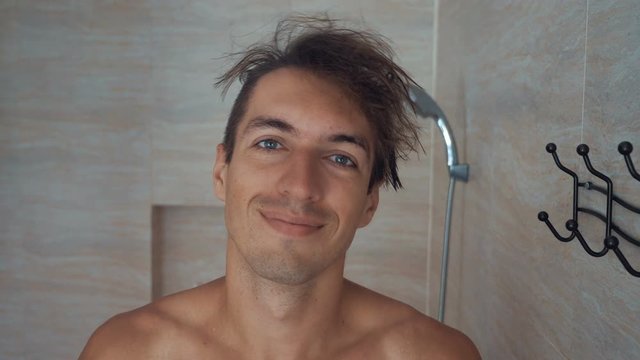 Young man is drying his hair by towel after douche in bathroom