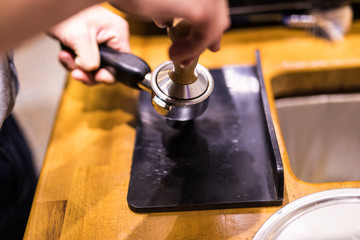 Barista Man is using a tamper to press freshly ground morning coffee into a coffee tablet