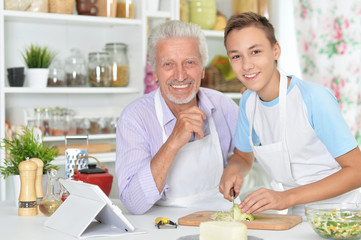 Portrait of senior man with grandson preparing dinner in kitchen
