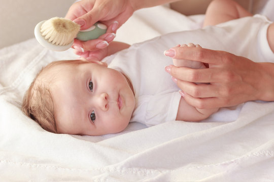 Baby and hands of mother with a baby hair brush, indoors, blurred background
