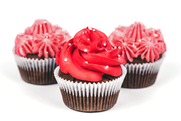 Three cupcakes with red and pink icing on isolated white background.