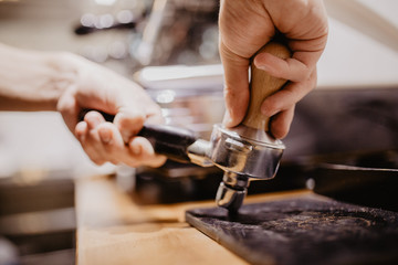 Barista grinding coffee beans using coffee machine, coffee grinder grinding freshly roasted make beans into powder.