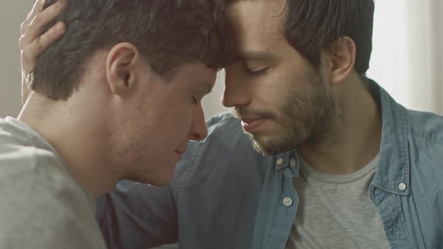 Cute Male Queer Couple Put Their Heads Together and Close Their Eyes. Sweet Gentle Loving Gay Relationship Moment. Room Has Modern Interior.