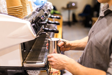 Barista man hands steaming milk for hot cappuccino with machine at the coffee shop in morning