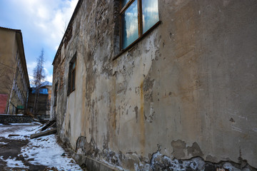 Reflection of blue sky in the window of old abandoned building with cracked wall near mountains.