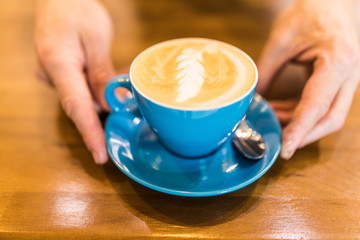 Hand holding cups of coffee with latte on wooden table, top view. Coffee break time concept