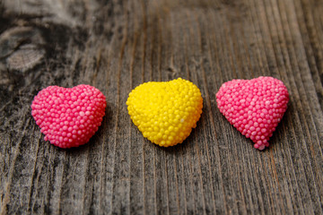 Three Multi colored gummy candy coated with sugar in the form of heart in on old wooden table