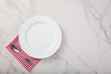 Empty plate on marble countertop with red plaid napkin.