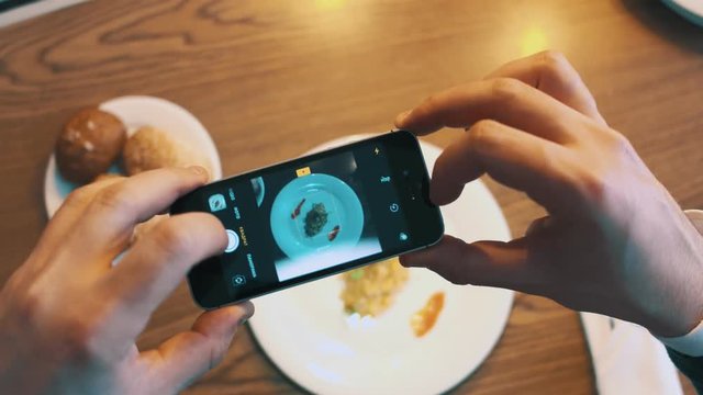 Male hand making photo food with mobile phone camera in restaurant close up