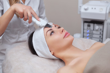 Obraz na płótnie Canvas The doctor-cosmetologist makes the ultrasound cleaning procedure of the facial skin of a beautiful, young woman in a beauty salon. Cosmetology and professional skin care.