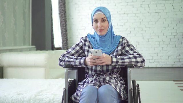beautiful young woman in hijab is disabled, wheelchair, uses the phone. looks into the camera