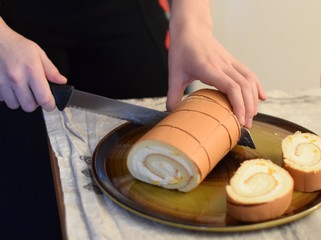 Frauenhände schneiden eine Biscuit-Rolle auf einer Kuchenpllatte auf einem festlich gedeckten Tisch - Woman hands cut a biscuit roll on a cake plate on a festively decorated table