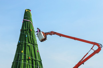 Worker on big crane during install and decoration ornament the christmas tree under blue sky