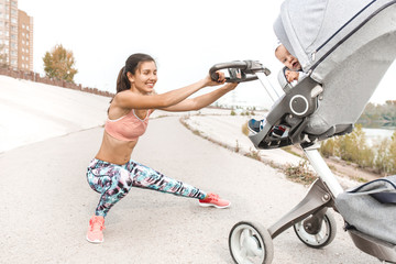 Active mother jogging. Jogging or power walking woman with pram at sunset. mom squats while walking with baby in stroller