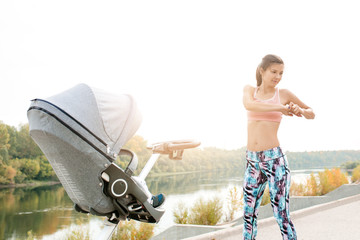 active mother is engaged in sports on the embankment of the river together with the child in a baby...