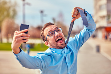 Funny businessman getting angry while using smartphone outdoors.