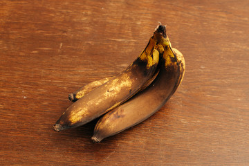 3 rotten and spoiled brown bananas on wooden background