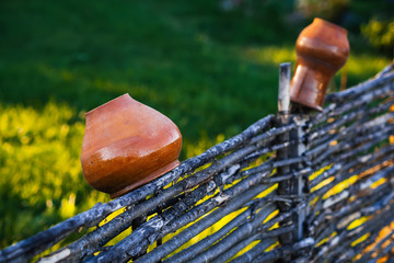 Clay pot and jug hanging on a wicker wooden fence