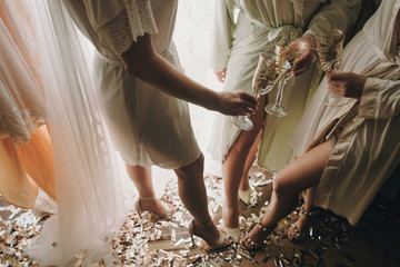 Bride with bridesmaids in silk robes toasting with champagne glasses and showing sexy legs,...